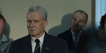 Movie still from “Chernobyl” (2019), directed by Johan Renck – A man in a suit and tie standing next to another man in a suit and tie; Medium shot, Low angle