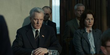 Movie still from “Chernobyl” (2019), directed by Johan Renck – A man in a suit and tie sitting at a table with other men; Medium shot, Over the shoulder angle