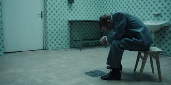 Movie still from “Chernobyl” (2019), directed by Johan Renck – A man kneeling on the ground in front of a tiled wall; Wide shot, High angle