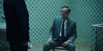 Movie still from “Chernobyl” (2019), directed by Johan Renck – A man sitting on a chair in front of a wall; Medium shot, Over the shoulder angle