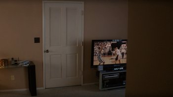 Movie still from “True Detective” (2014), created by Issa López – A television set in a living room next to a white door; Wide shot, High angle