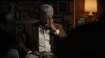 Movie still from “True Detective” (2014), created by Issa López – An older man in a brown suit sitting in front of a brick wall; Close Up shot, Over the shoulder angle