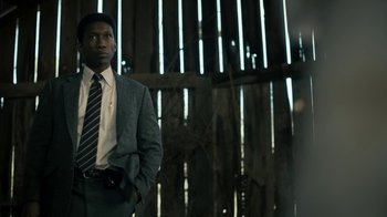 Movie still from “True Detective” (2014), created by Issa López – A man in a suit and tie standing in front of a wooden fence; Medium shot, Low angle