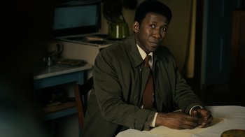Movie still from “True Detective” (2014), created by Issa López – A man sitting at a table in front of a computer; Medium shot, High angle