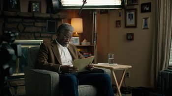 Movie still from “True Detective” (2014), created by Issa López – An older man sitting in a chair looking at a paper; Medium shot, Over the shoulder angle