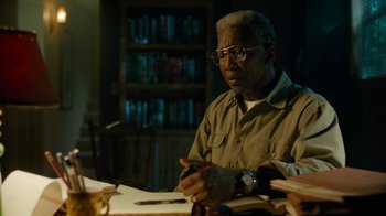 Movie still from “True Detective” (2014), created by Issa López – An older man sitting at a table writing on a piece of paper; Close Up shot, High angle