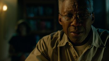 Movie still from “True Detective” (2014), created by Issa López – An older man wearing glasses sitting at a table; Close Up shot, Low angle