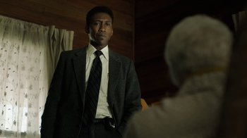 Movie still from “True Detective” (2014), created by Issa López – A man wearing a suit and tie standing next to another man; Close Up shot, Over the shoulder angle