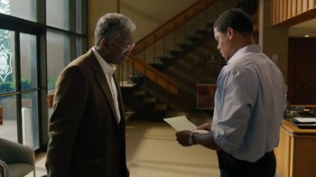 Movie still from “True Detective” (2014), created by Issa López – Two men standing next to each other holding papers; Medium shot, Over the shoulder angle