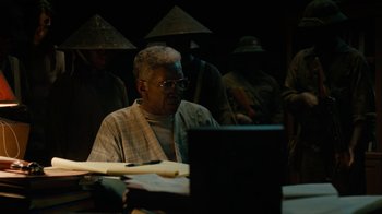 Movie still from “True Detective” (2014), created by Issa López – An older man sitting at a table in front of an open laptop computer; Medium shot, High angle