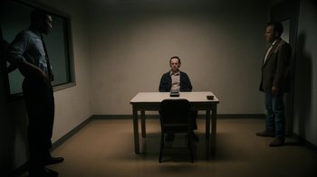 Movie still from “True Detective” (2014), created by Issa López – A man sitting at a table in front of a cell phone; Wide shot, High angle