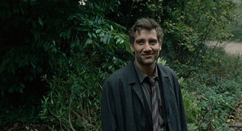 Movie still from “Children of Men” (2006), directed by Alfonso Cuarón – A man wearing a suit and tie standing in front of trees; Close Up shot, Low angle
