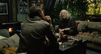 Movie still from “Children of Men” (2006), directed by Alfonso Cuarón – Two men sitting at a table talking to each other; Medium shot, Over the shoulder angle