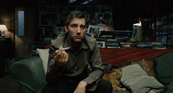Movie still from “Children of Men” (2006), directed by Alfonso Cuarón – A man sitting on a couch with a cat in the background; Medium shot, Low angle