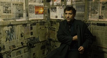 Movie still from “Children of Men” (2006), directed by Alfonso Cuarón – A man sitting in front of a bunch of newspapers; Medium shot, Over the shoulder angle