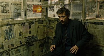 Movie still from “Children of Men” (2006), directed by Alfonso Cuarón – A man sitting in front of a bunch of newspapers; Medium shot, High angle