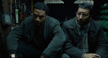 Movie still from “Children of Men” (2006), directed by Alfonso Cuarón – A couple of men sitting next to each other on a couch; Medium shot, Low angle