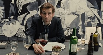 Movie still from “Children of Men” (2006), directed by Alfonso Cuarón – A man sitting at a table with a glass of red wine; Medium shot, Over the shoulder angle
