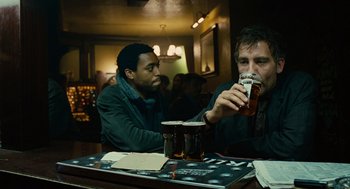 Movie still from “Children of Men” (2006), directed by Alfonso Cuarón – Two men sitting at a table drinking beer; Medium shot, Over the shoulder angle