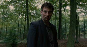 Movie still from “Children of Men” (2006), directed by Alfonso Cuarón – A man in a black suit standing in the woods; Medium shot, Low angle