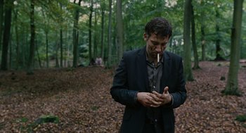 Movie still from “Children of Men” (2006), directed by Alfonso Cuarón – A man smoking a cigarette in the middle of a forest; Medium shot, Low angle