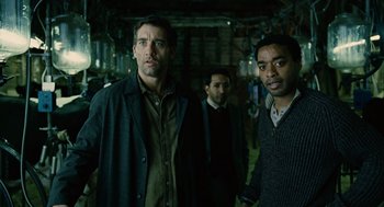 Movie still from “Children of Men” (2006), directed by Alfonso Cuarón – A group of men standing next to each other in a room; Medium shot, Low angle