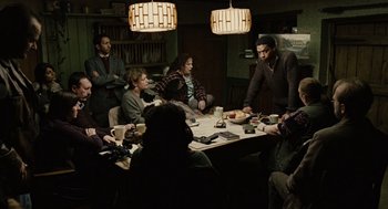 Movie still from “Children of Men” (2006), directed by Alfonso Cuarón – A group of people sitting around a table in a room; Wide shot, High angle