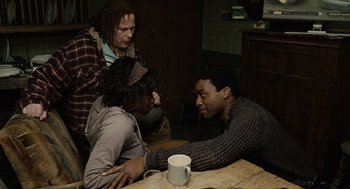 Movie still from “Children of Men” (2006), directed by Alfonso Cuarón – A group of people sitting at a table with a cup of coffee; Medium shot, High angle