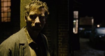 Movie still from “Children of Men” (2006), directed by Alfonso Cuarón – A man with curly hair standing in a dark room; Close Up shot, Over the shoulder angle