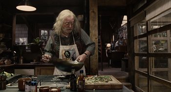 Movie still from “Children of Men” (2006), directed by Alfonso Cuarón – An older man in a kitchen preparing food; Medium shot, High angle