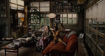 Movie still from “Children of Men” (2006), directed by Alfonso Cuarón – Two women sitting on a couch in a living room; Wide shot, High angle