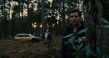 Movie still from “Children of Men” (2006), directed by Alfonso Cuarón – A man and a woman standing in the woods near a car; Medium shot, Low angle
