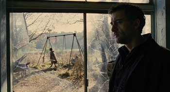 Movie still from “Children of Men” (2006), directed by Alfonso Cuarón – A man standing in front of a swing set looking out of a window; Medium shot, Over the shoulder angle