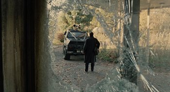 Movie still from “Children of Men” (2006), directed by Alfonso Cuarón – A man standing in front of an armored vehicle; Wide shot, Over the shoulder angle
