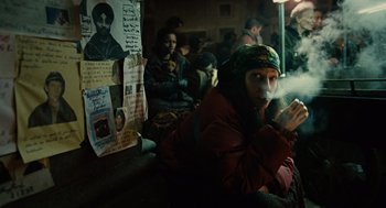 Movie still from “Children of Men” (2006), directed by Alfonso Cuarón – A group of people sitting in a room with posters on the wall; Medium shot, Over the shoulder angle