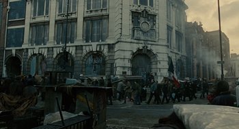 Movie still from “Children of Men” (2006), directed by Alfonso Cuarón – A group of people walking down a street near a building; Wide shot, Low angle