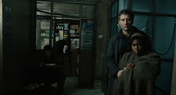 Movie still from “Children of Men” (2006), directed by Alfonso Cuarón – A man and a woman standing next to each other in a room; Medium shot, Low angle