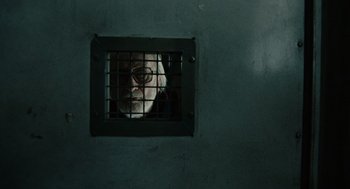 Movie still from “Children of Men” (2006), directed by Alfonso Cuarón – A man with a mask is looking out of a jail cell; Close Up shot, Over the shoulder angle