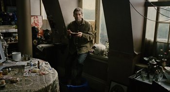 Movie still from “Children of Men” (2006), directed by Alfonso Cuarón – A man standing in front of a window holding a cell phone; Wide shot, High angle
