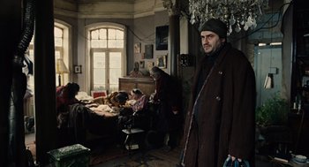 Movie still from “Children of Men” (2006), directed by Alfonso Cuarón – A man standing in front of a bed in a room; Wide shot, Low angle