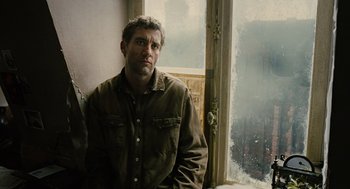 Movie still from “Children of Men” (2006), directed by Alfonso Cuarón – A man standing in front of a window looking sad; Medium shot, Over the shoulder angle