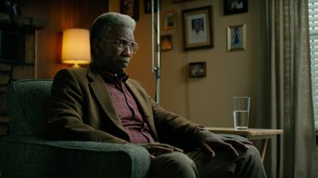 Movie still from “True Detective” (2014), created by Issa López – An older man sitting on a couch in a living room; Close Up shot, Over the shoulder angle
