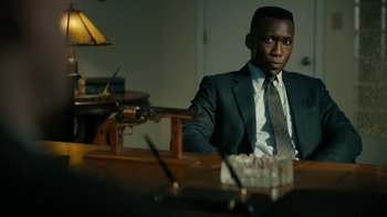 Movie still from “True Detective” (2014), created by Issa López – A man sitting at a table in a suit and tie; Close Up shot, Over the shoulder angle