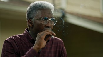 Movie still from “True Detective” (2014), created by Issa López – An older man smoking a cigarette while wearing glasses; Close Up shot, Over the shoulder angle