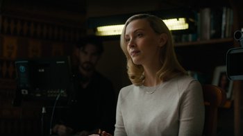Movie still from “True Detective” (2014), created by Issa López – A woman is looking at the camera while a man sits in the background; Close Up shot, Over the shoulder angle