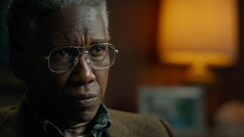 Movie still from “True Detective” (2014), created by Issa López – An older man wearing glasses looking at the camera; Close Up shot, Over the shoulder angle
