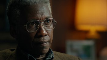 Movie still from “True Detective” (2014), created by Issa López – An older man wearing glasses looking at the camera; Close Up shot, Over the shoulder angle