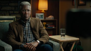 Movie still from “True Detective” (2014), created by Issa López – An older man sitting in a chair in front of a table with a glass of water on it; Close Up shot, Over the shoulder angle
