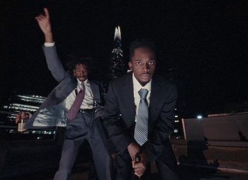 Movie still from “Sam Akpro - Death By Entertainment” (2023), directed by Pedro Takahashi – Medium shot, Low angle