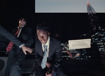 Movie still from “Sam Akpro - Death By Entertainment” (2023), directed by Pedro Takahashi – Medium shot, Low angle